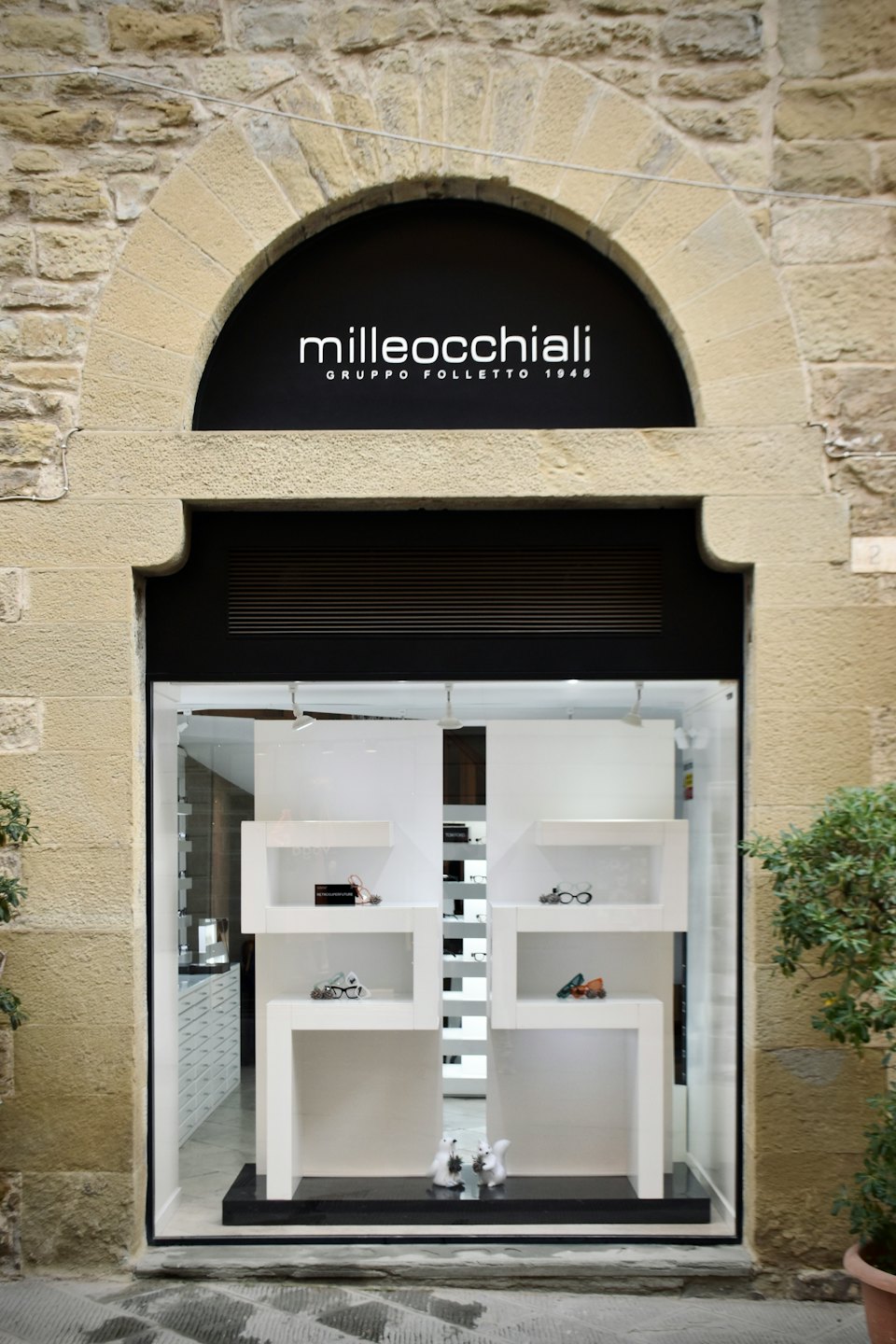 Eyeglasses displayed in an optical shop with a stone arched entryway.